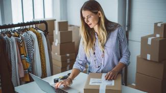 Woman scrolling on her computer while packaging a box